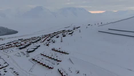 drone view in svalbard flying over longyearbyen town showing houses in a snowy area with mountains in the horizon in norway