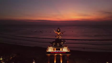 drone view showcases kuta beach at sunset with the towering baruna statue, a striking cultural landmark that blends traditional balinese artistry with the golden glow of the coastal horizon