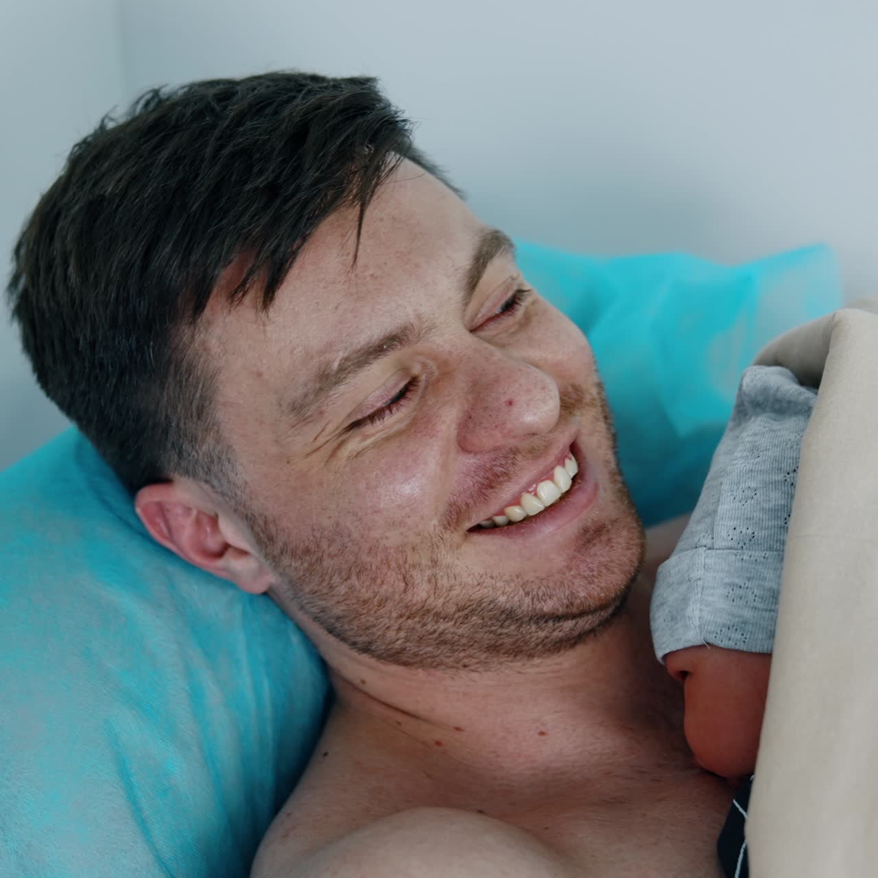 Happy Caucasian man is excited to hold his newborn baby. Father is having tears in his eyes holding his child carefully. Top view