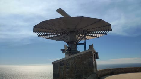 radar for maritime traffic control at the top of the mountain with the reflective sea in the background on a sunny summer day, shot blocked from below