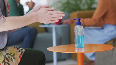 Mid-section-of-woman-sanitizing-her-hands-at-office