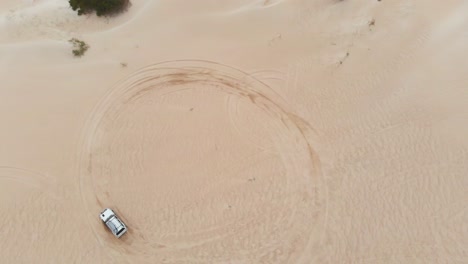 top down view of 4x4 car driving circles on sand dunes at western australia, aerial