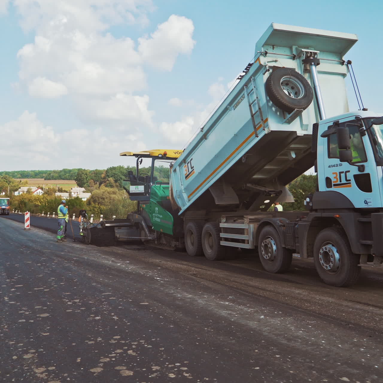 New asphalt road in the countryside. Laying of asphalt carried out by workers and pavers. Asphalt paver machine on a road construction site.