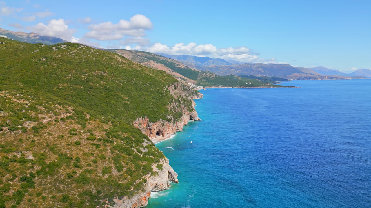 Aerial drone shot flying high over steep cliff covered with green vegetation along the seaside in Gjipe beach, Albania on a sunny day