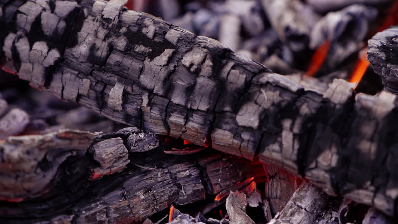 Wooden logs glowing in fire. Firewood coal in the fireplace. Texture of burned wooden logs. Slow motion shot. Close-up.
