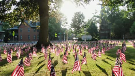 establishing shot of small town in united states with lawn decorated with american flags during dramatic morning sunlight through trees, church in distance