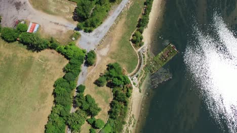 an aerial view over a park on a sunny day. the water in the bay is calm and reflective. there are green trees along the edges of the water. the camera looks straight down while moving forward