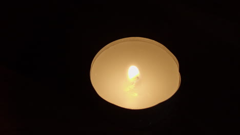 Dark-close-up:-Hand-with-burning-match-lights-tea-candle-in-black-room