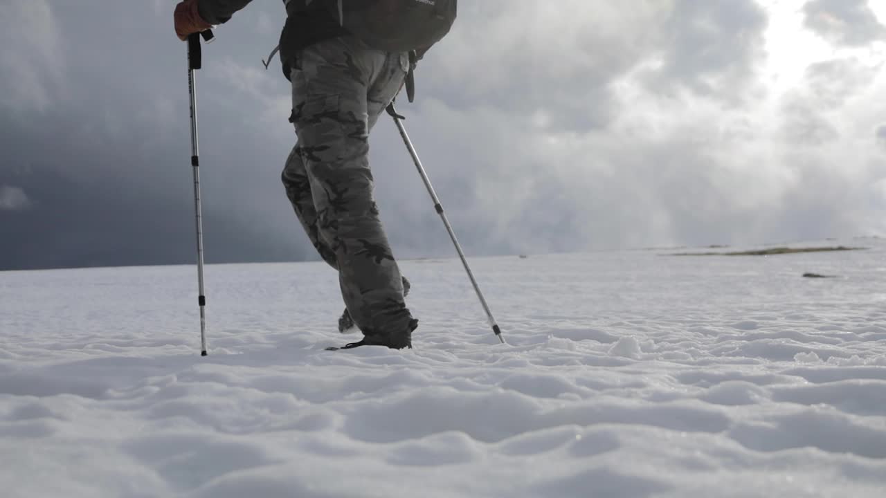 Slow motion, single person with hiking poles walking in thick snow. Low angle, view of legs only