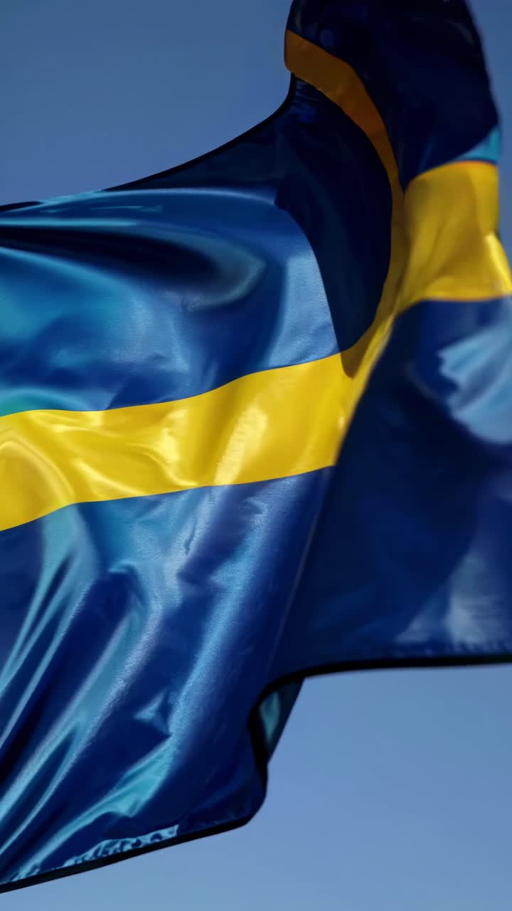 Close-up video shot of a Swedish flag waving against a clear blue sky, capturing the vibrant yellow