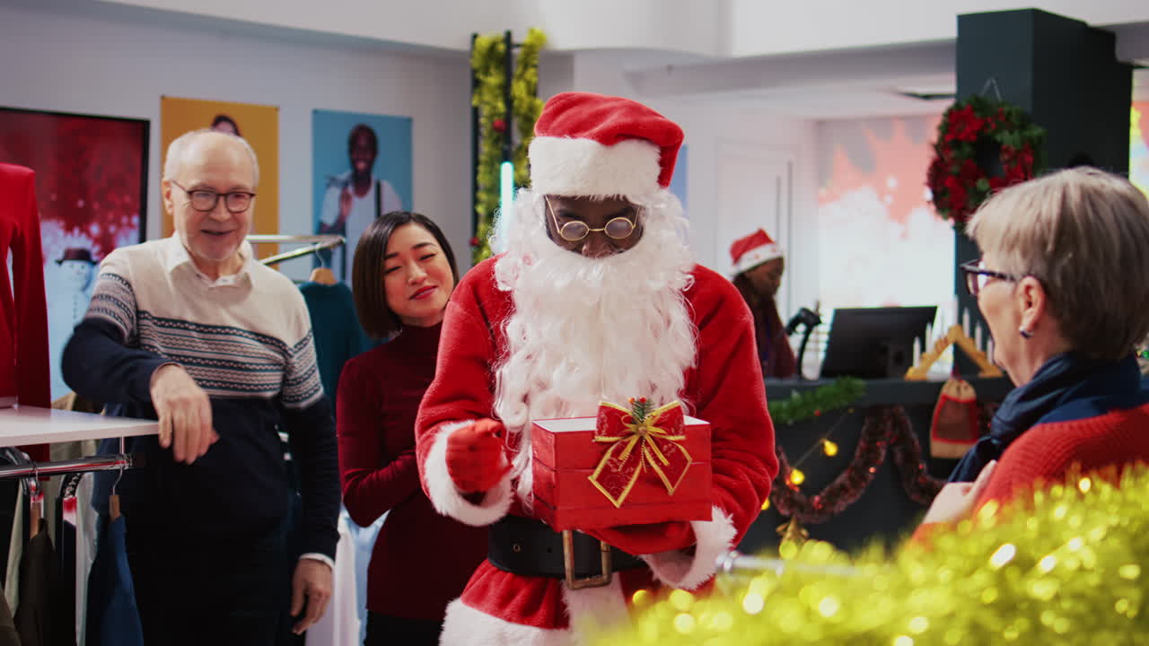 Funcionário vestido de Papai Noel segurando uma caixa de presente que serve como recipiente para bilhetes de rifa, misturando-os para escolher um vencedor aleatório entre clientes alegres em uma loja de moda decorada para o Natal.