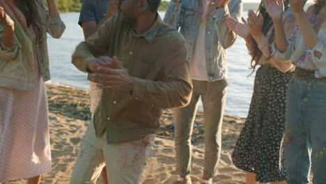 joyful middle eastern man covered with gulal paint dancing with friends outdoors at beach party