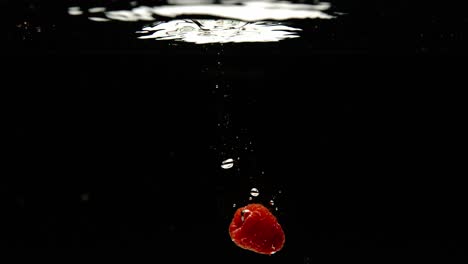 super slow motion of falling fresh raspberries into water on black background