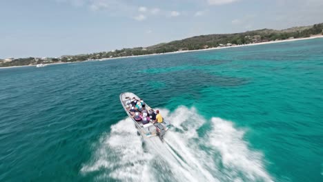 Acrobatic-drone-flying-over-tourist-boat-navigating-in-blue-sea-along-Playa-Ensenada-beach-in-Dominican-Republic