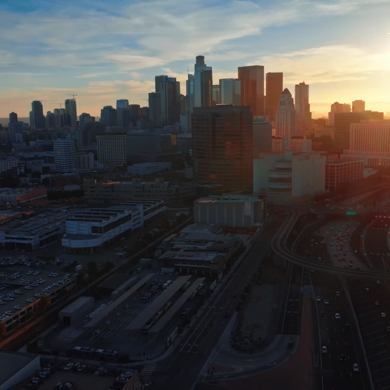 Excellent scenery of Los Angeles downtown in the evening. Numerous cars moving quickly by the highways. Bright sun at backdrop