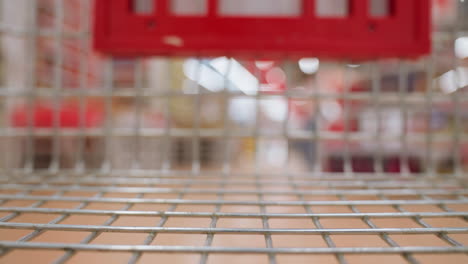 un carrito de compras en movimiento dentro de un centro comercial, mostrando la cuadrícula metálica del carrito y el fondo borroso del interior del centro comercial. capturado con una cámara de mano
