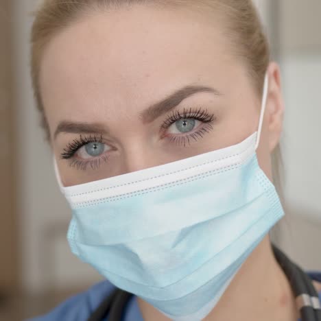 Portrait-of-young-female-doctor-in-medical-mask--blue-coat-and-stethoscope