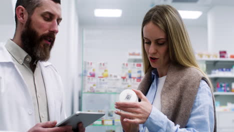 Hombre-Con-Tableta-Hablando-Con-Una-Mujer-Joven-En-La-Farmacia.