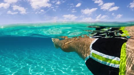 first person view of man legs and feet floating on breathtaking clear and transparent ocean water of exotic island