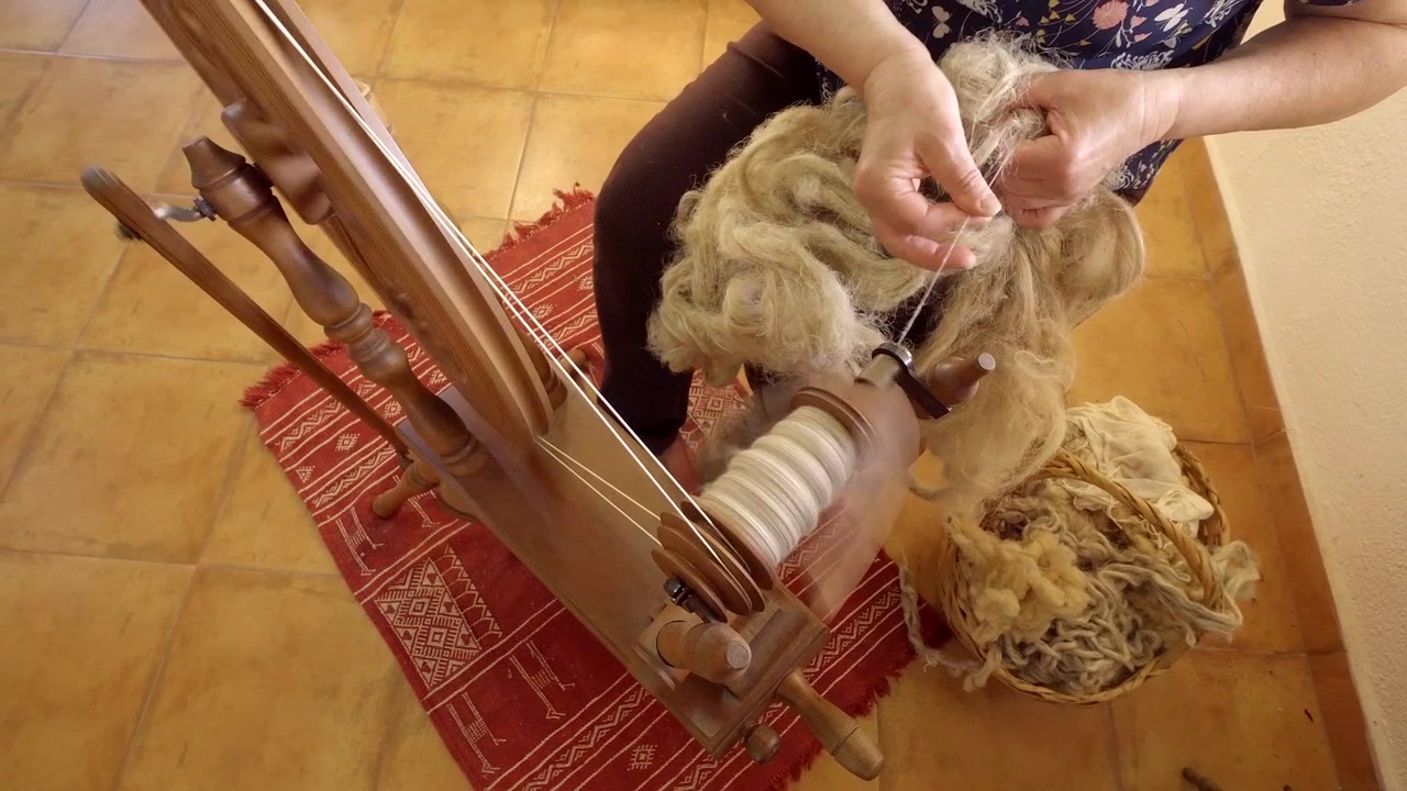 Close Up Of A Woman Making Yarn From Wool On A Foot Operated Spinning Wheel.