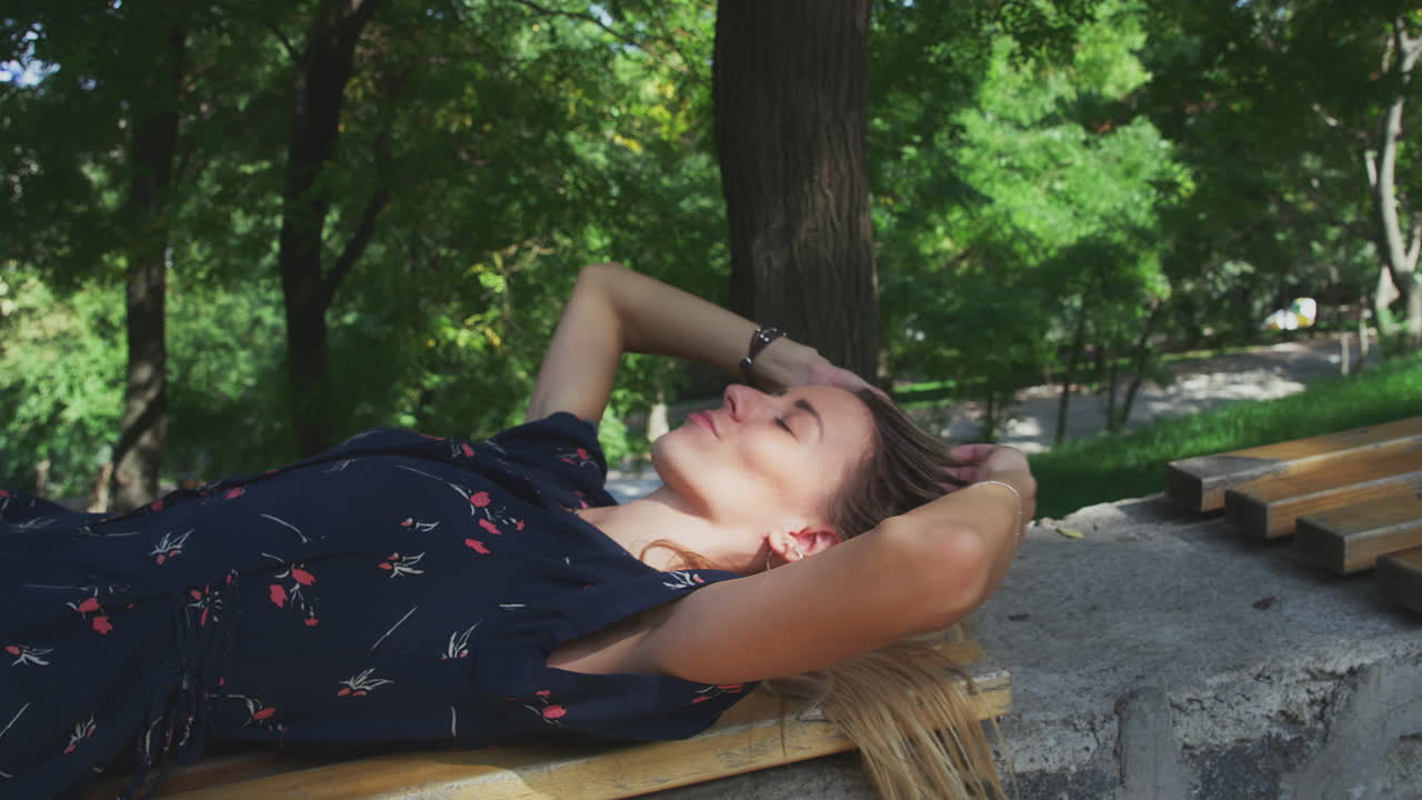 태양 그늘에서 공원 벤치에 누워 휴식을 취하는 젊은 여성이 팔을 뻗어 눈을 뜨다