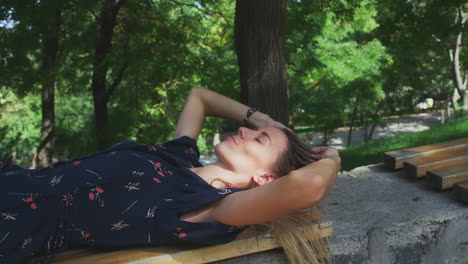 mujer joven relajándose acostada en un banco del parque a la sombra del sol estira los brazos y abre los ojos