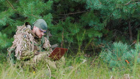 a man in military uniform sitting in the woods enjoying the pclaptop