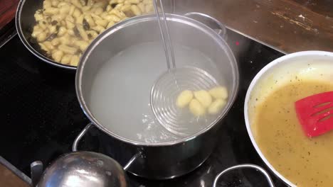 detail shot of boiling gnocchi pasta getting taken out of the pot and put into a pan for cooking, birds eye view