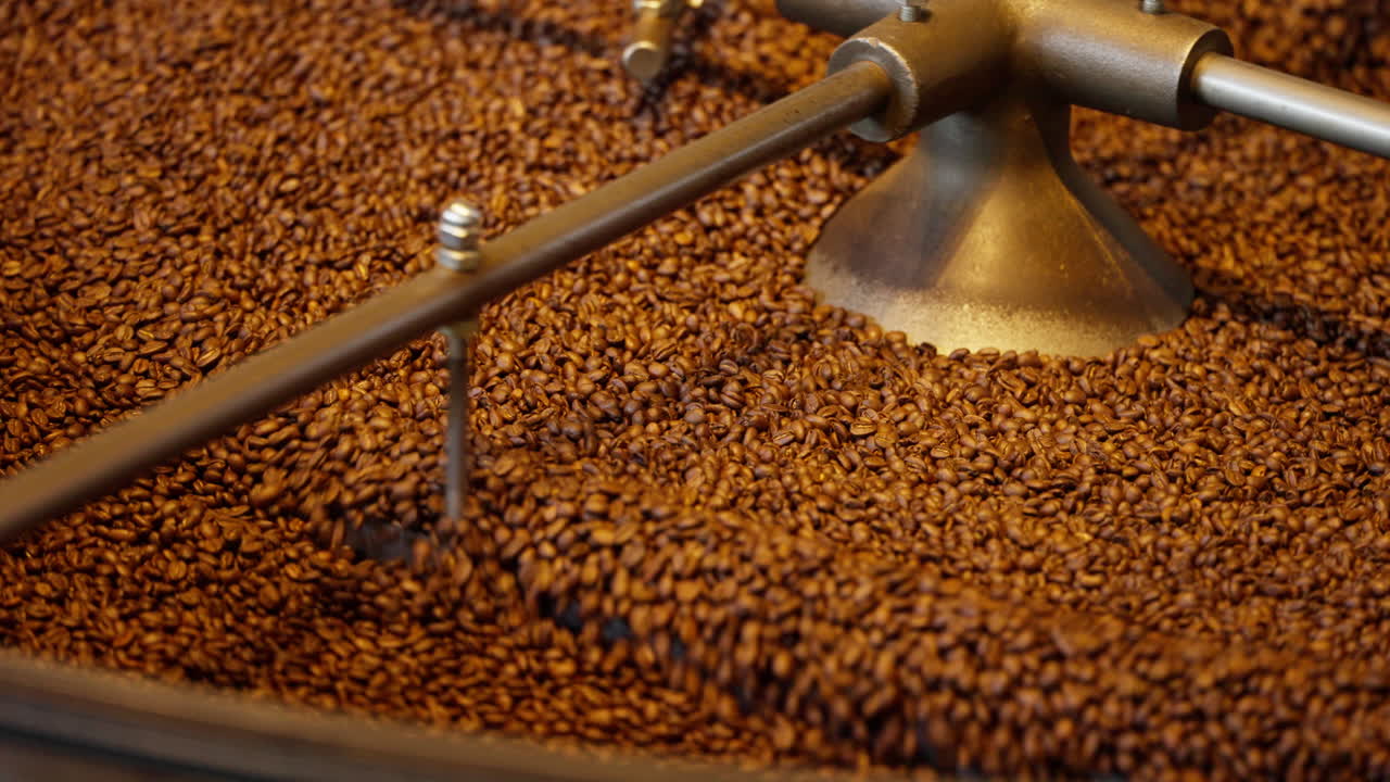 Close-up of coffee beans roasting in an industrial drum roaster, stirring under heat. Warm cinematic texture highlights fresh aroma and specialty coffee production