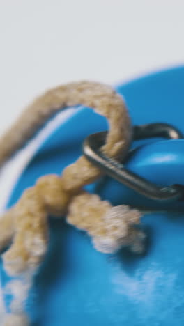 motion above blue rubber basin plug with brown rustic rope lies on clean white surface extreme close view