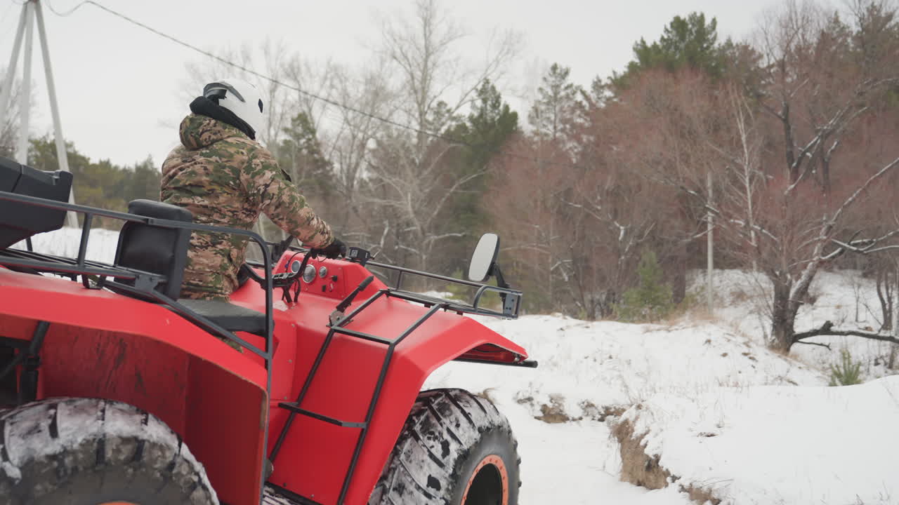 Quad ATV rosso in una foresta innevata, un pilota mimetico sale e avvia il veicolo, pneumatici con battistrada profondo mordono la neve fresca, il motore romba e genera vapore dallo scarico; un'inquadratura ravvicinata evidenzia l'aderenza e il controllo, in stile cacciatore.