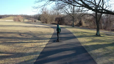 An-aerial-tracking-of-a-man-on-an-electric-skateboard-in-an-empty-park-on-a-sunny-day