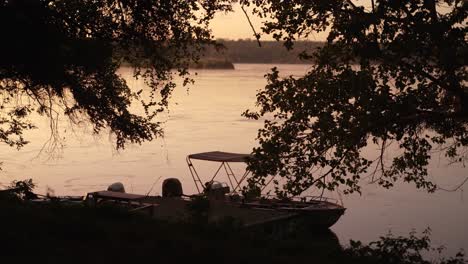 Fishing-boat-sitting-on-the-banks-of-a-flowing-river-at-sunrise-or-sunset-golden-hour