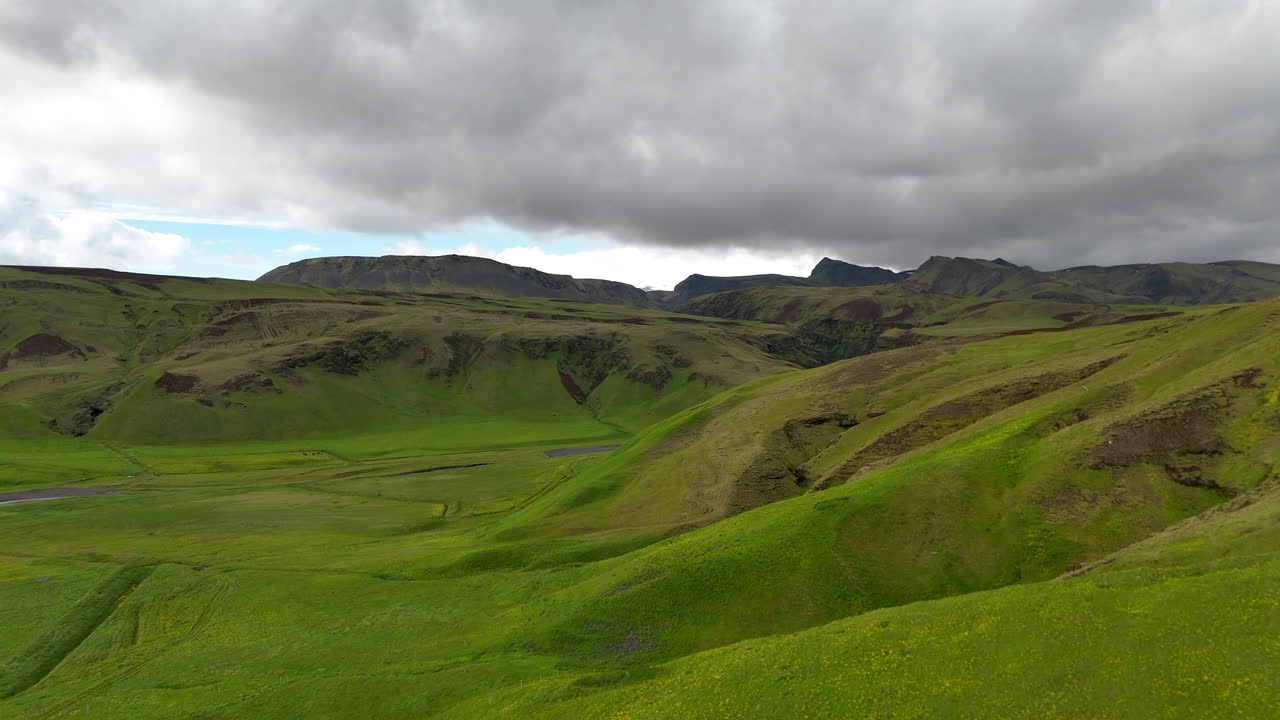 Aerial drone view of the lush Myrdalshreppur canyon with steep moss-covered cliffs, winding river and dramatic volcanic terrain under dark storm clouds in southern Iceland