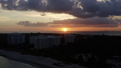 Right-trucking-aerial-drone-shot-of-a-stunning-yellow-golden-ocean-sunset-with-tropical-greenery-below-from-Crandon-Park-in-Key-Biscayne-outside-of-Miami,-Florida-on-a-warm-sunny-summer-evening