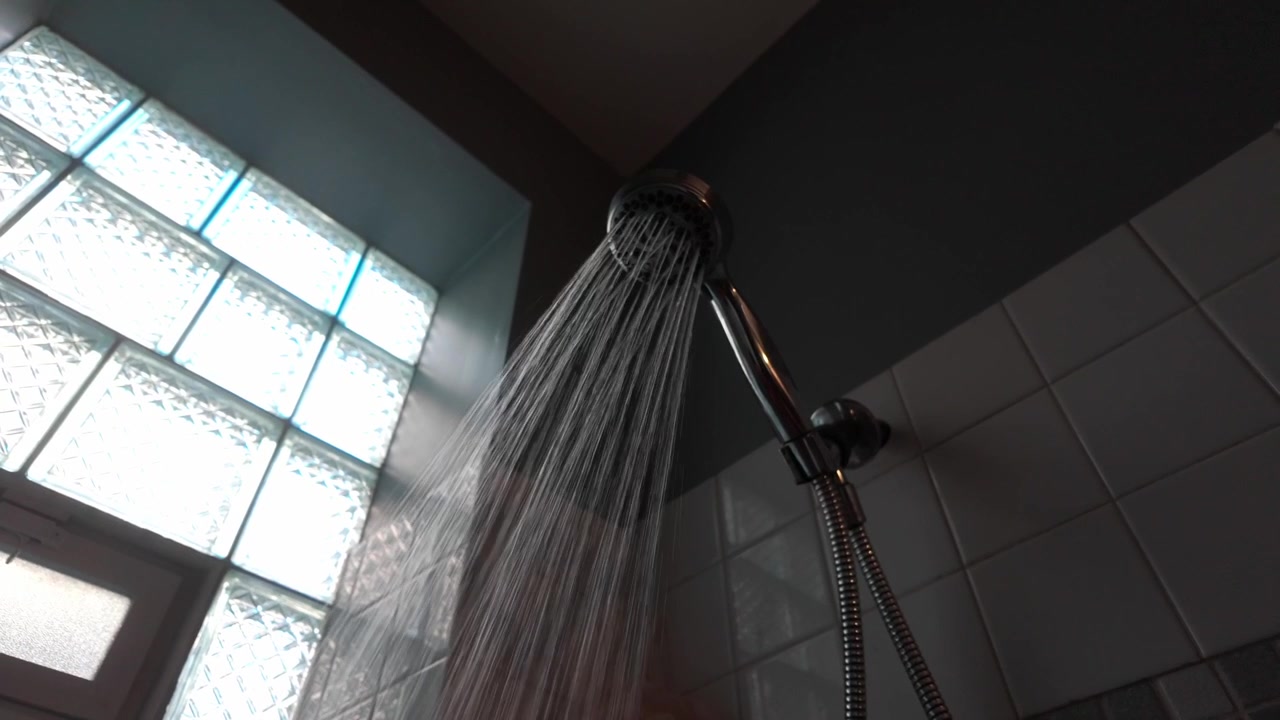 A running shower raining down water in a bathroom with a sunny window.