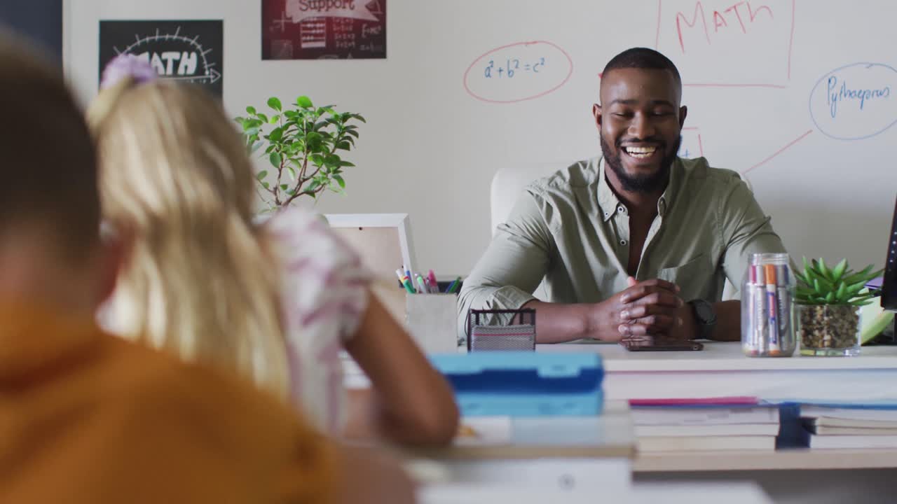 Video of happy african american male teacher sitting at desk during math lesson