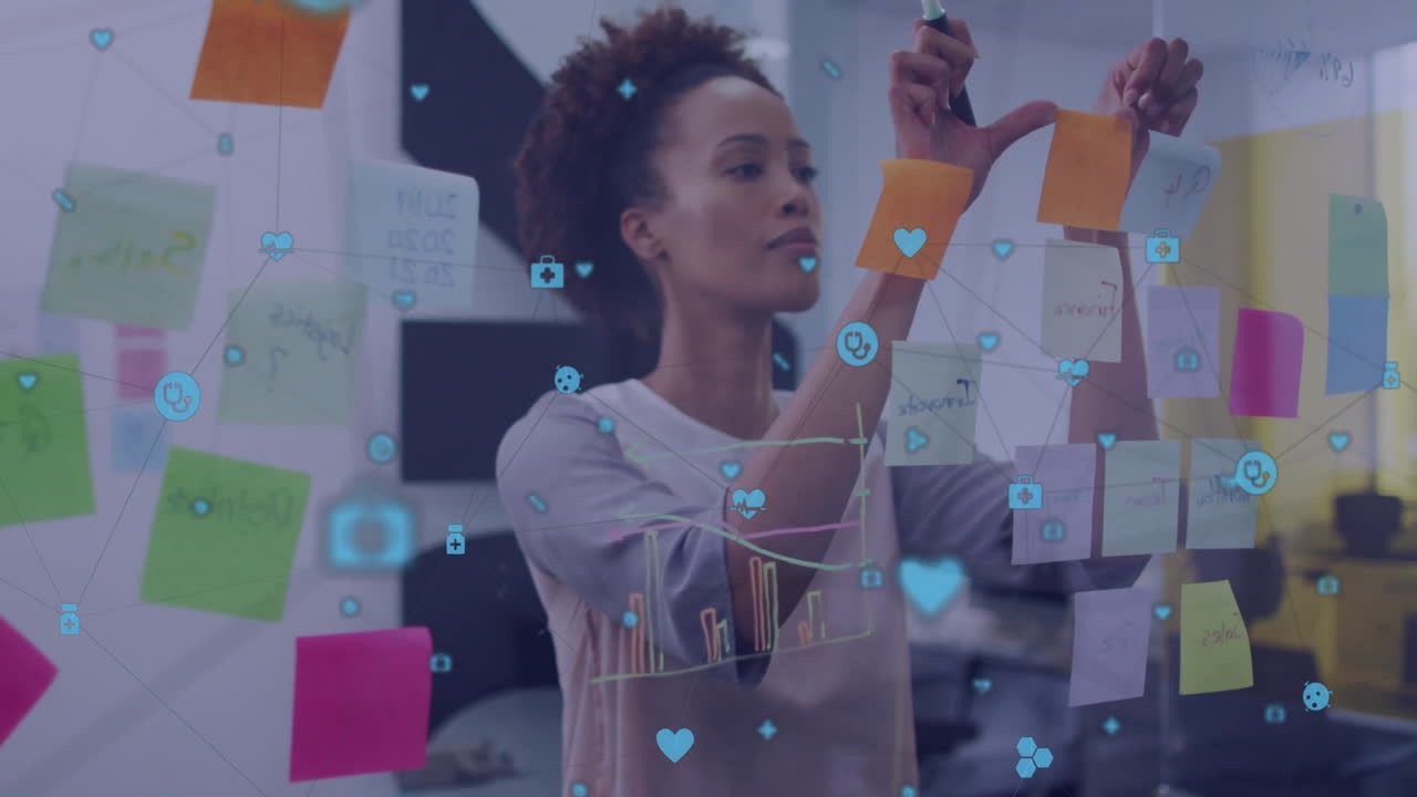 Animation of network of media icons over biracial casual businesswoman brainstorming at office