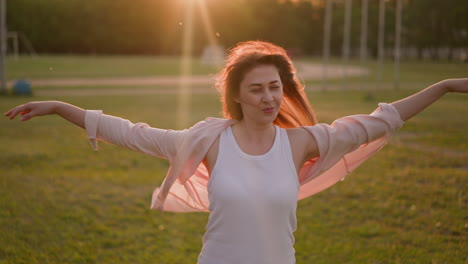 positive woman raises hands enjoying strong wind on meadow