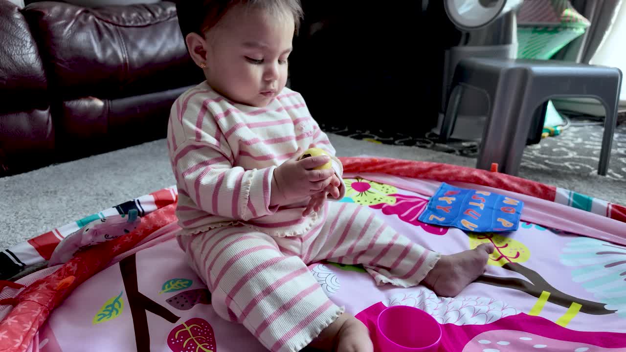 South Asian baby discovering a yellow toy while playing on an activity mat