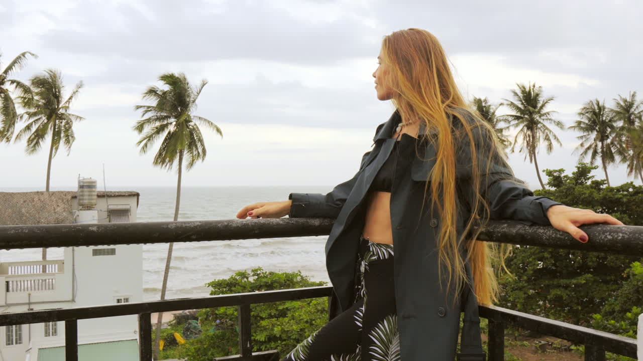 Female Model Poses on Balcony with Tropical Background of Palm Trees and the Ocean