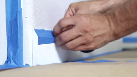 4k, painter using masking blue tape to secure baseboard, moulding. preparation for room painting.