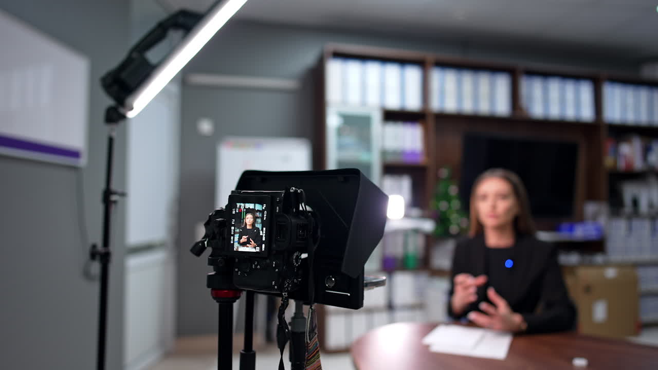 Brunette female talks to camera recording a video. Modern blog creator in the studio. Blurred backdrop.