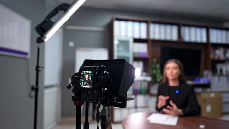 brunette female talks to camera recording a video. modern blog creator in the studio. blurred backdrop.