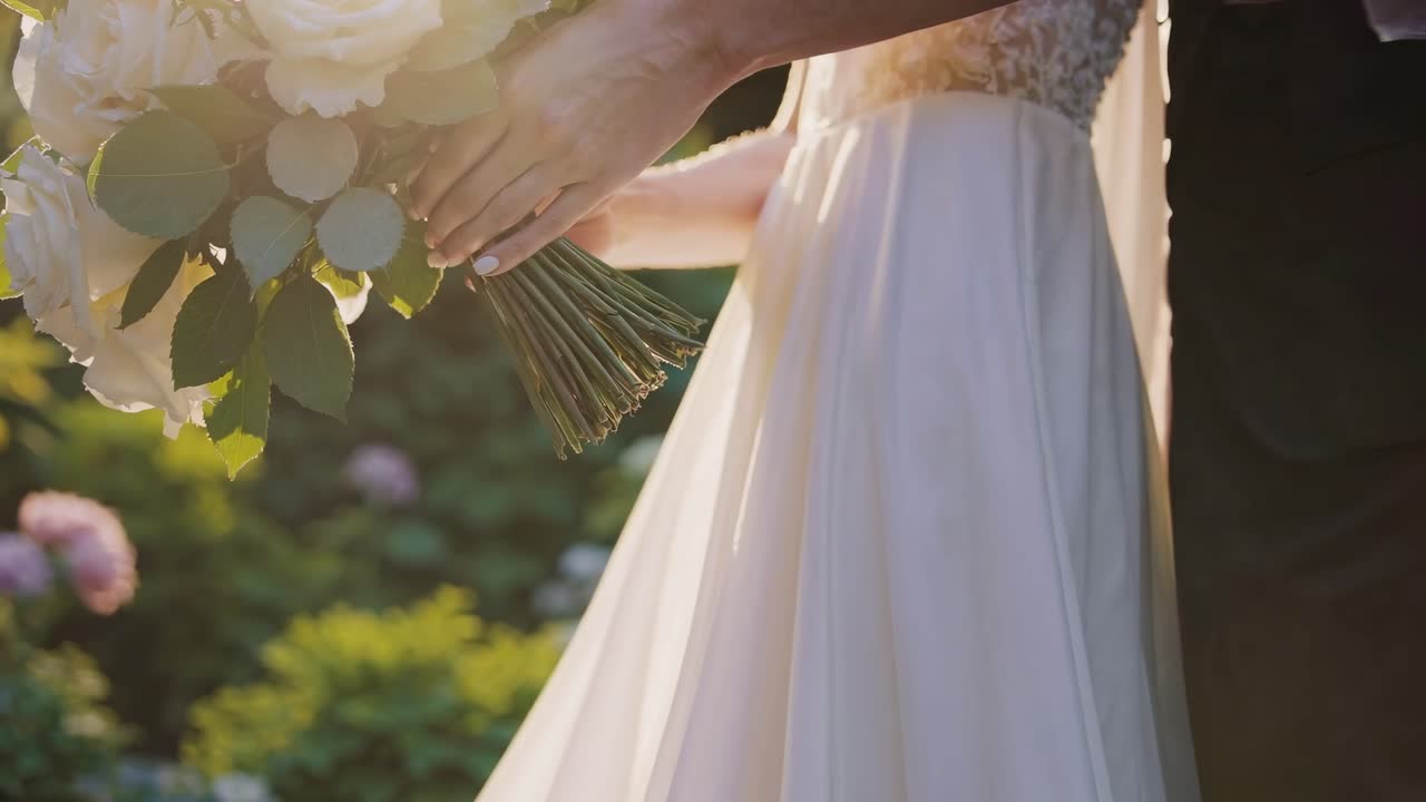 Sposi che tengono un bouquet da sposa di rose bianche in un giardino soleggiato.
