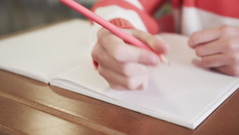 young girl writing in notebook with pink pencil at school desk, focusing intently