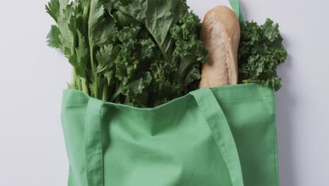 Video-of-green-canvas-bag-with-parsley,-kale-and-baguette,-copy-space-on-white-background