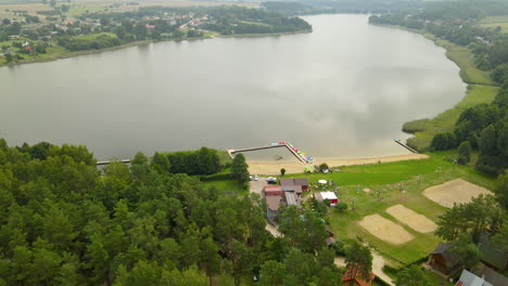 Inclinación-Aérea-Desde-El-Paisaje-Del-Lago-Hartowiec-Hasta-Hoteles-Privados-Equipados-Para-Deportes-Acuáticos-De-Verano-Como-Kayak,-Piragüismo,-Pedaleo-Y-Pesca-Rodeados-De-Un-Denso-Bosque-Verde,-Polonia