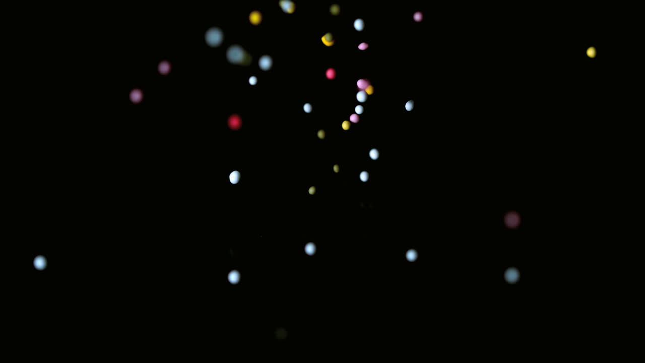 Colourful sprinkles pouring onto black surface