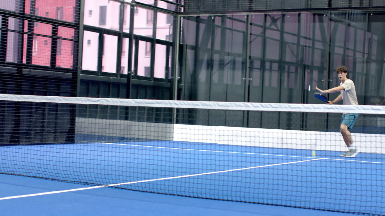 Young man playing padel tennis on indoor court, holding racket and smiling